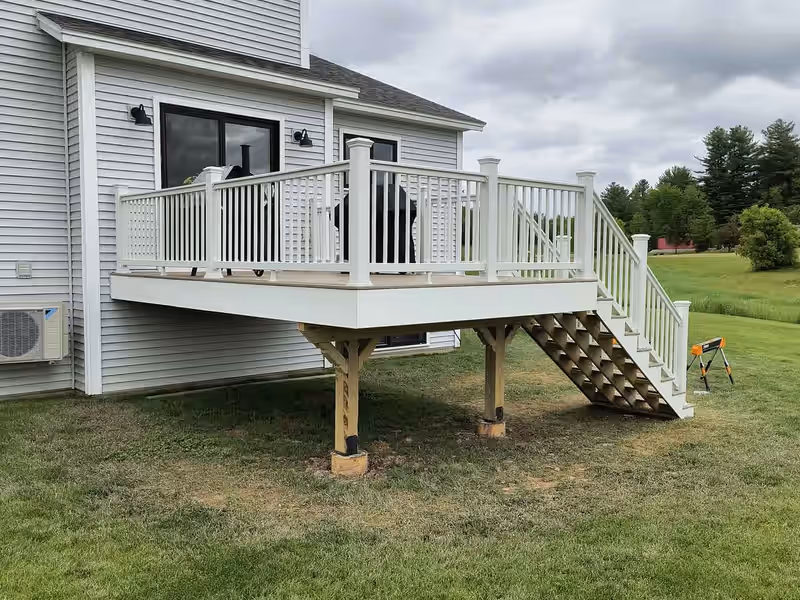 Raised attached deck with white vinyl railing and tan composite decking on a Vermont home, built by Empirical Renovations