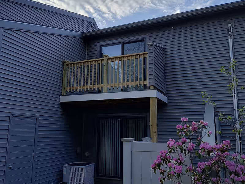 Second-story balcony deck with new pressure-treated railing cantilevered above a doorway on a Vermont home, built by Empirical Renovations