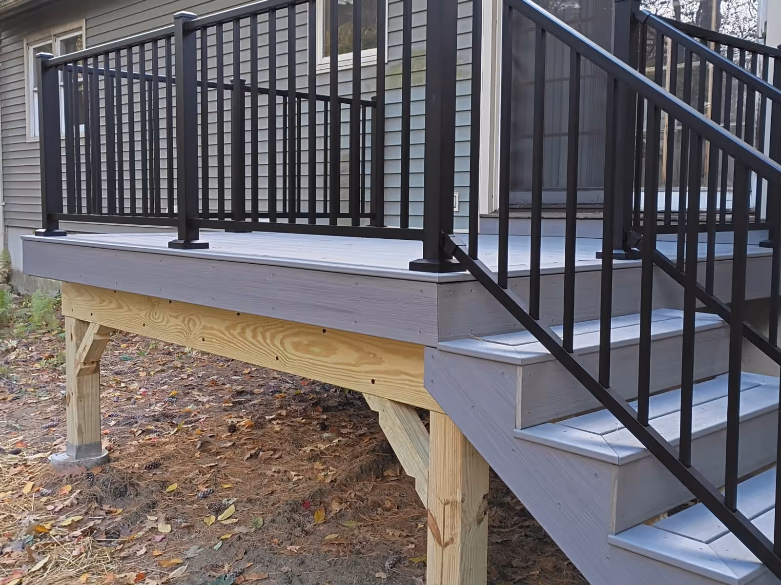 The same deck finished in Millstone Trex with black Trex Select railings and stairs down to the yard, Milton VT
