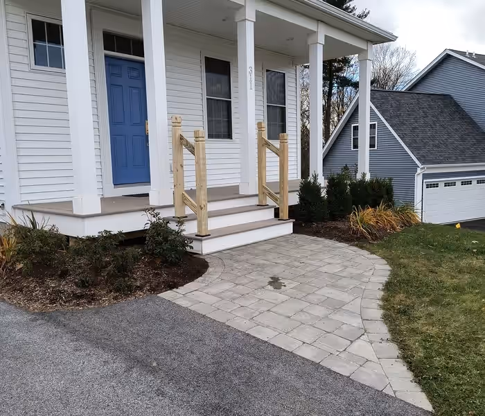 New pressure-treated stair railings on a white front entry porch with a blue door, built by Empirical Renovations in Vermont