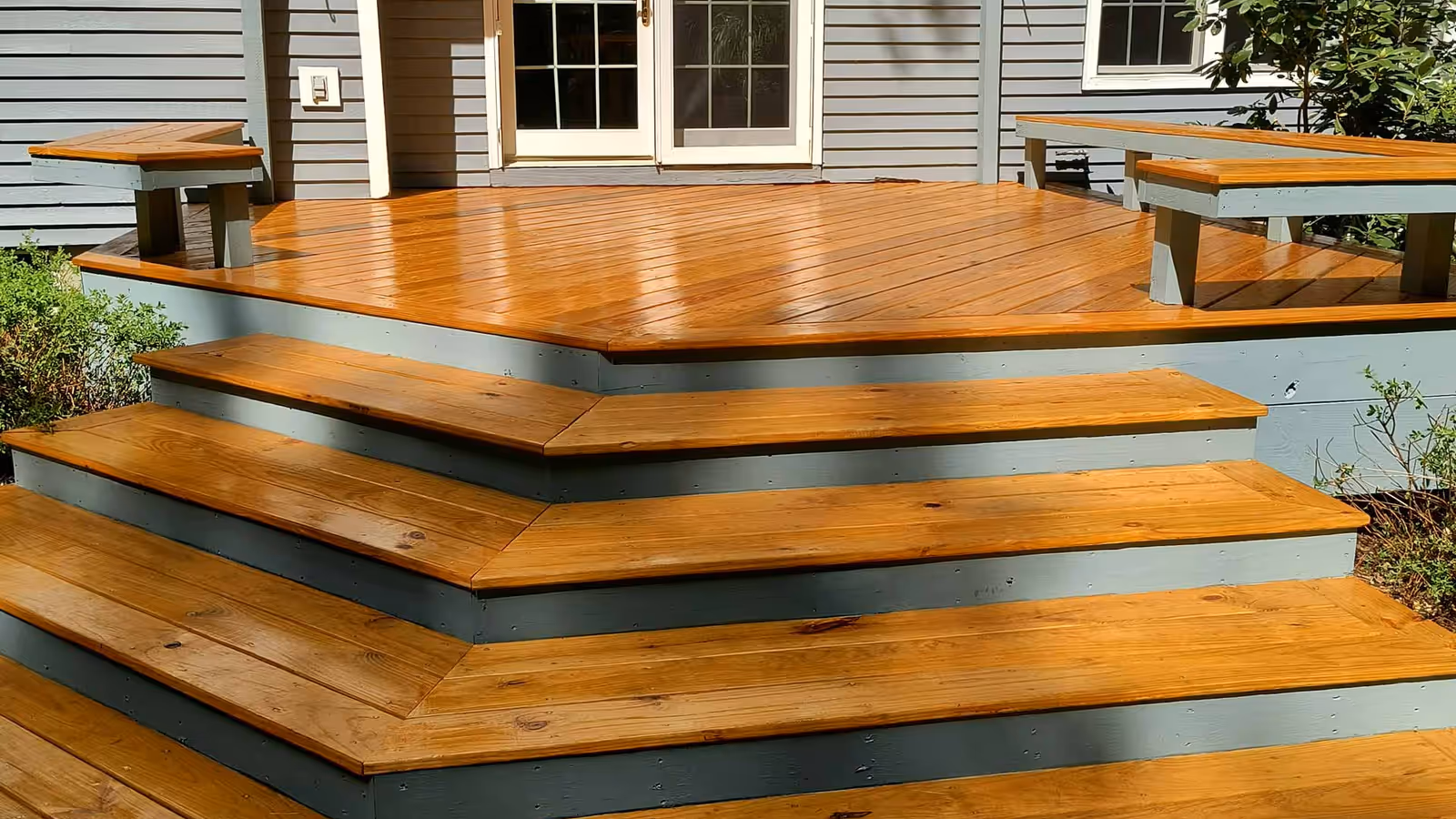 Deck and wraparound steps finished in a warm amber stain with painted gray risers by Empirical Renovations in Vermont
