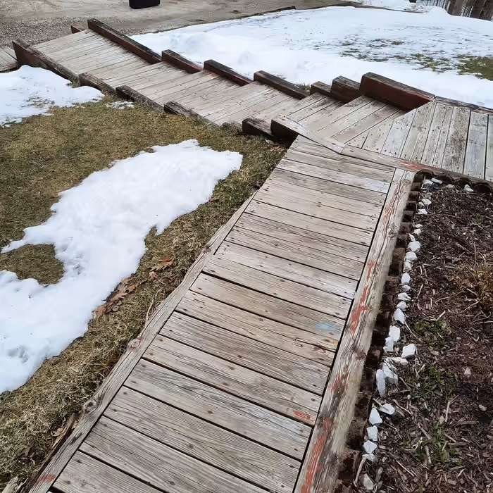 Weathered wooden walkway and steps with grayed boards and traces of old red stain, snow on the ground, before rebuilding at a Vermont home