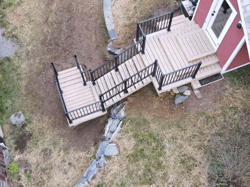 Aerial view of a front entry deck with tan composite decking and black aluminum railing at a red Vermont home, built by Empirical Renovations