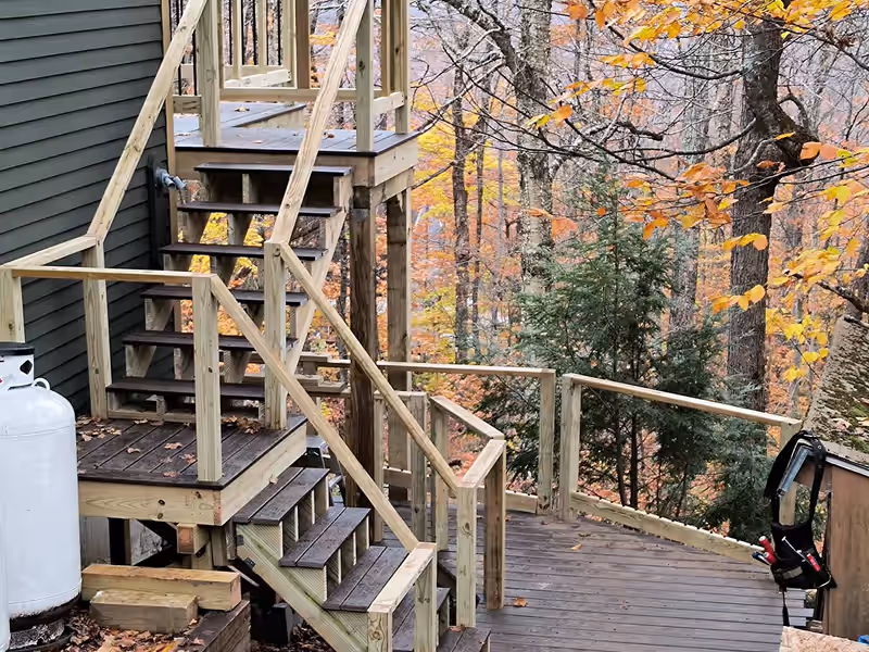 Multilevel deck with new pressure-treated stairs stepping down a wooded Vermont hillside, built by Empirical Renovations