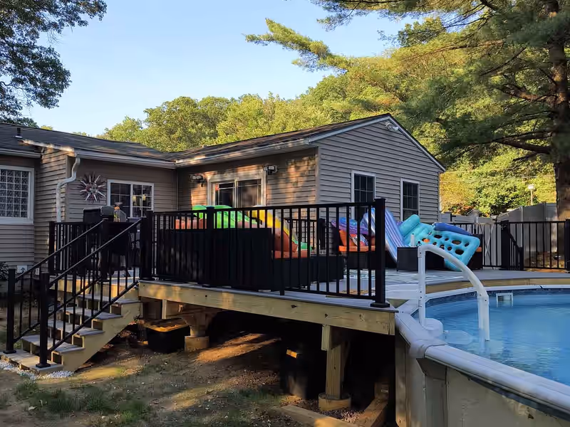 Deck built alongside an above-ground pool with black aluminum railing on a Vermont property, by Empirical Renovations