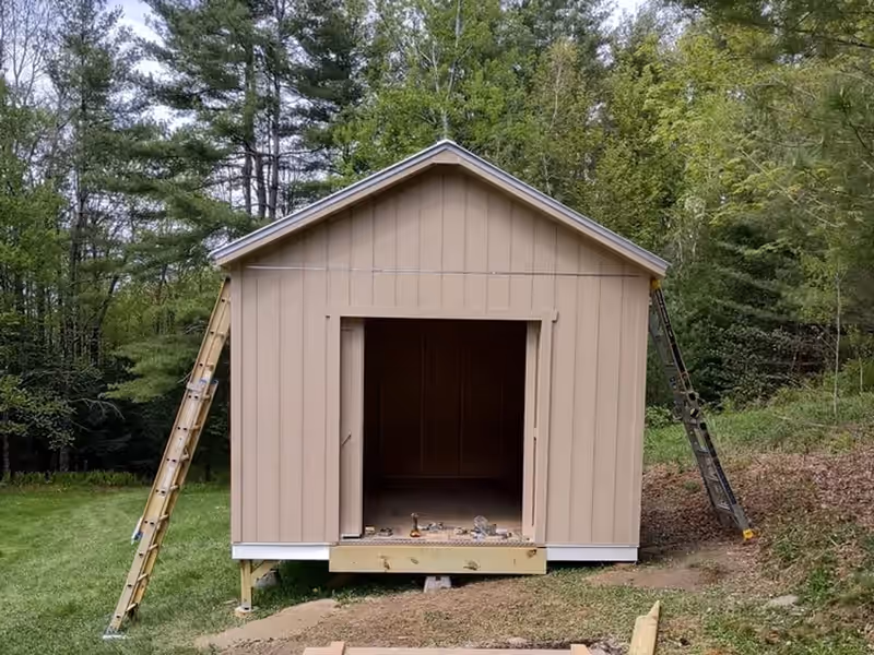 Shed framed and sided on site by Empirical Renovations at a wooded Vermont property, ladders up and the wide door opening still open