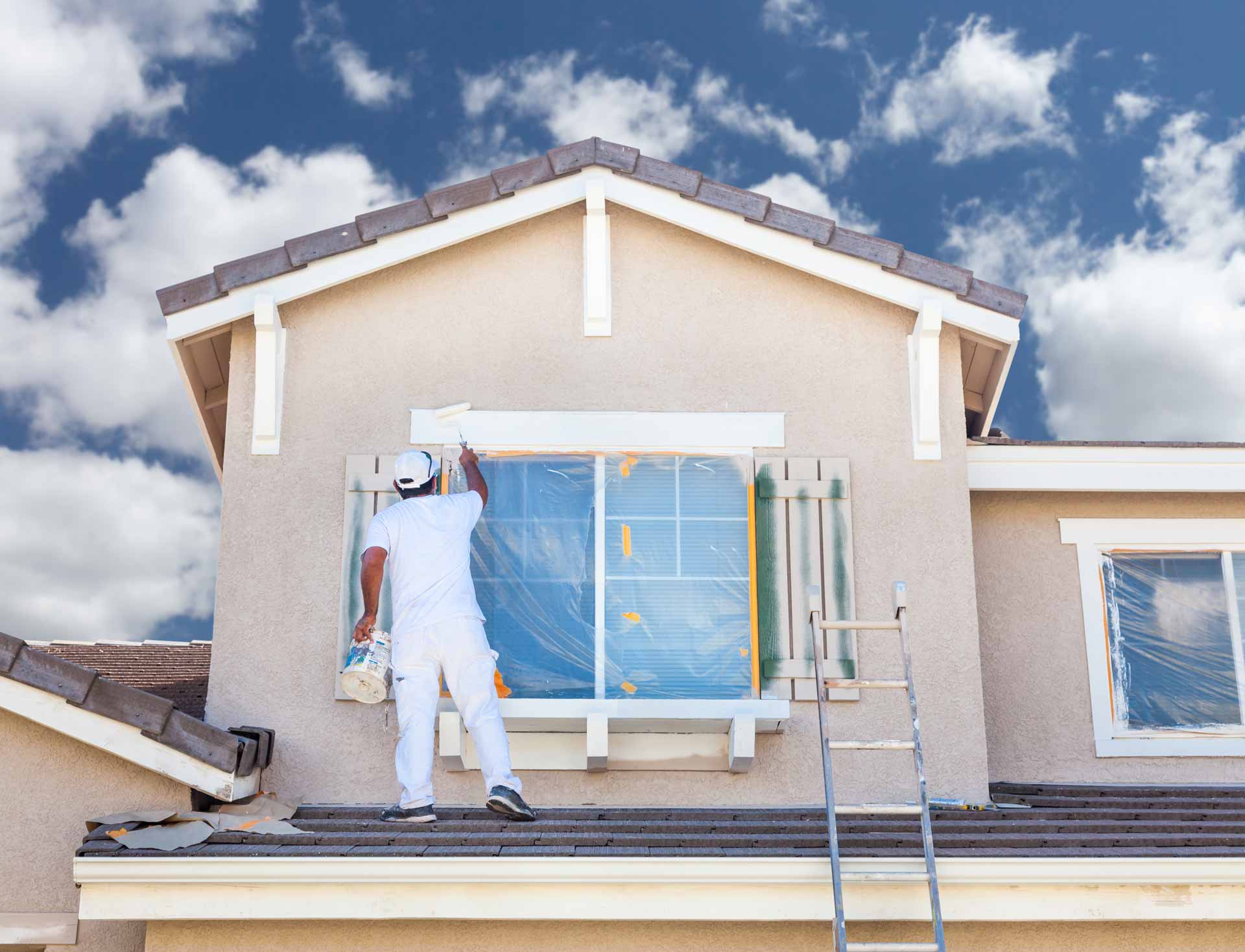 Man standing on roof to paint window shutters