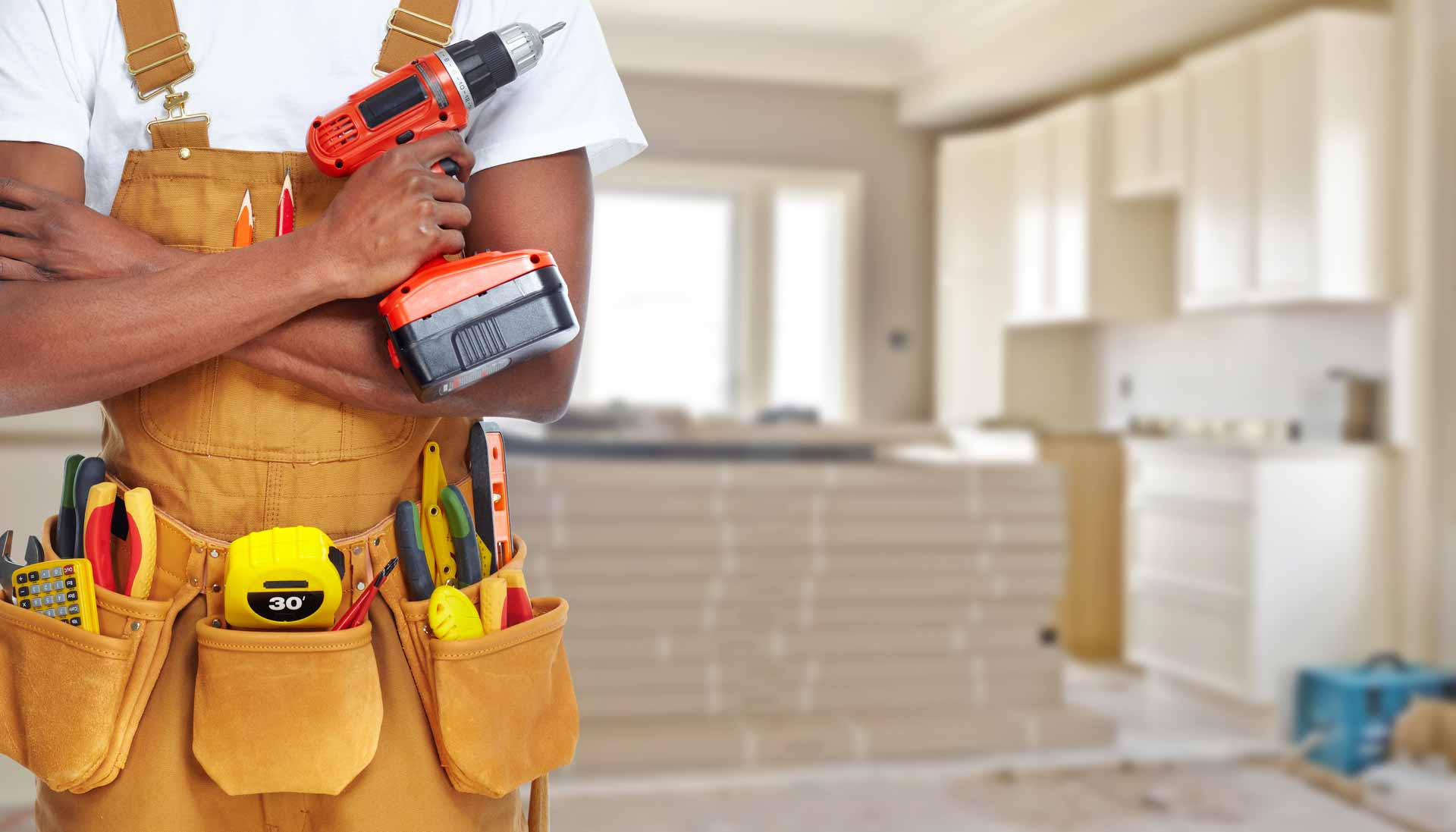 Man wearing an apron and utility belt full of construction tools holding a power drill on home renovation job site